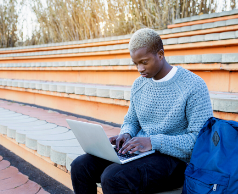 Black male student sitting on bleachers with laptop